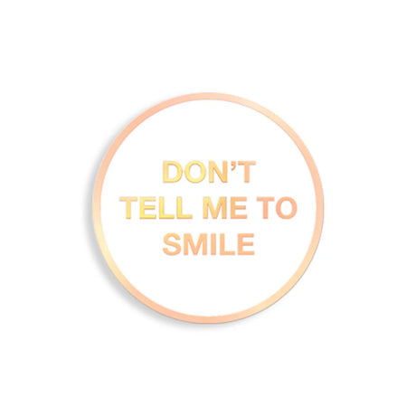 Round enamel pin with “Don’t Tell Me To Smile” in gold text