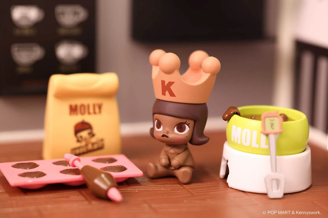 Molly figure wearing brown crown next to bag of chocolate flour, piping chocolate into molds