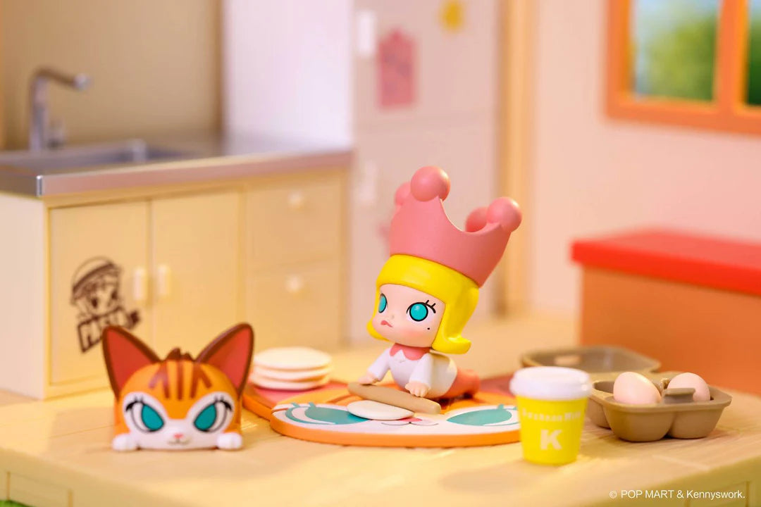 Molly figure with pink crown rolling dough on table while cat figure peeks from countertop