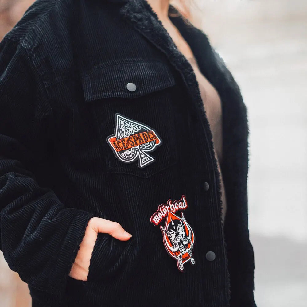 Person wearing Motörhead patches on black jacket with Ace of Spades and Snaggletooth visible