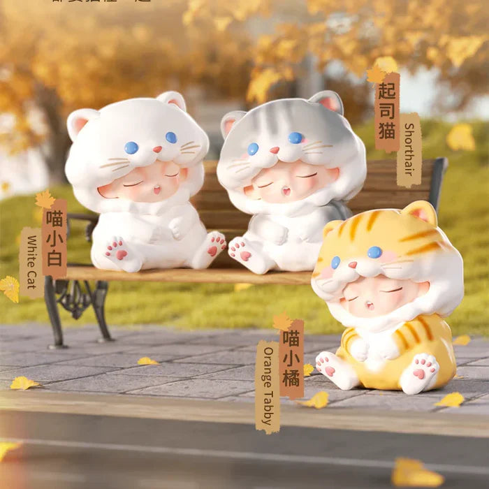 White cat, shorthair cat, and orange tabby Yumo figures sitting on park bench.