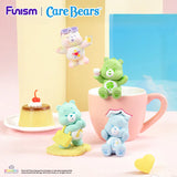 Care Bears Little Things Cubby Face Series figures displayed beside a mug and dessert