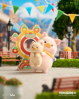 LuLu The Piggy hugging a cat friend beside a colorful carnival ferris wheel attraction