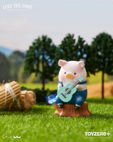 LuLu The Piggy sitting on a tree stump playing a blue guitar in a countryside setting