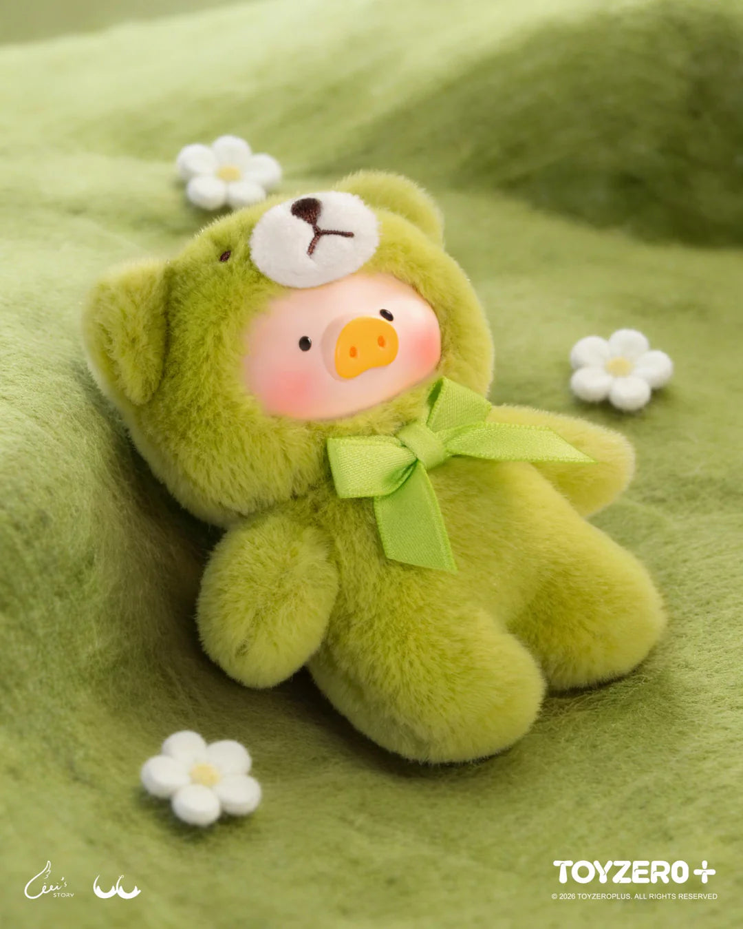 LuLu The Piggy in a green teddy bear outfit resting on a grassy nature-themed display