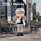 Molinta vinyl figure in school-style outfit with bread standing near a city café.