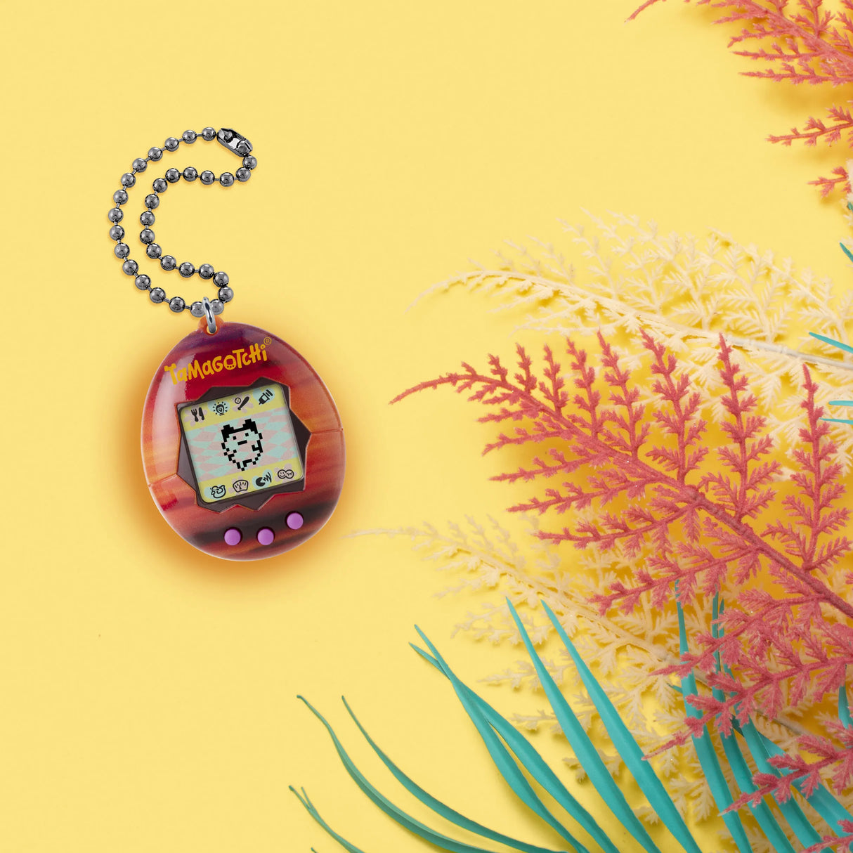 Tamagotchi Sunset edition on yellow background with tropical plants.