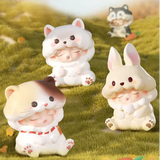 White cat, calico cat, and beige bunny Yumo figures sitting on grassy field.
