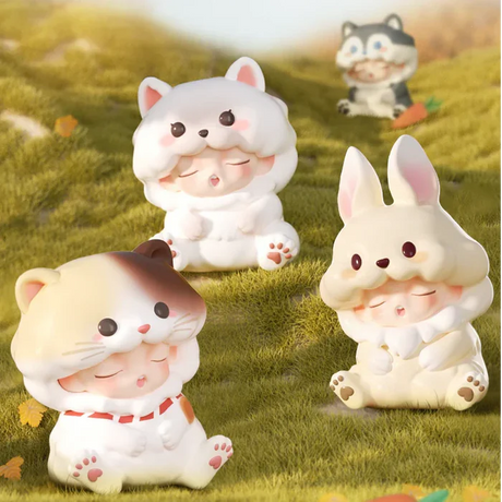 White cat, calico cat, and beige bunny Yumo figures sitting on grassy field.